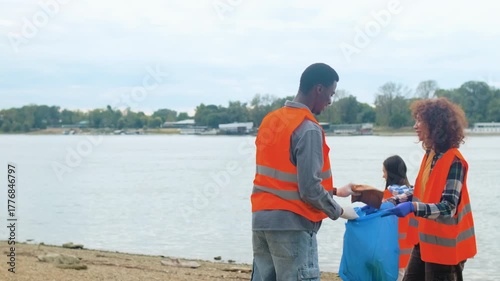 Group of volunteers cleaning river bank collecting plastic waste together.