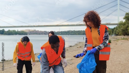 Group of volunteers cleaning river bank collecting plastic waste together.