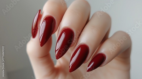 Elegant hand with long, pointed nails painted in glossy deep red polish, showcasing meticulous nail art and highlighting beauty and fashion trends in manicured hands