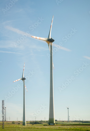Tall modern wind turbines turning on a clear sunny day in a rural open landscape generating renewable clean green wind power energy under a blue sky horizon. 