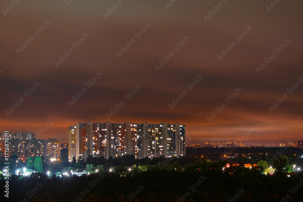 Naklejka premium Kyiv cityscape presents a night panorama, featuring modern apartment buildings with many illuminated windows creating a vibrant urban glow against a dark, cloudy sky