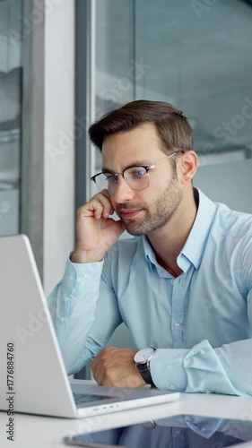 Confused young trader businessman looking disappointed at laptop pc computer screen having stress. Tired European business man holding hand near temples, feeling stressed sitting in office. Vertical