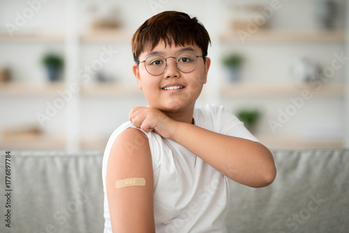 A cheerful asian boy with glasses displays a bandage on his arm after receiving a coronavirus vaccine. This closeup portrait captures a moment of health awareness during the pandemic. Free Download A cheerful asian boy with glasses displays a bandage on his arm after receiving a coronavirus vaccine. This closeup portrait captures a moment of health awareness during the pandemic. - GFXLoad