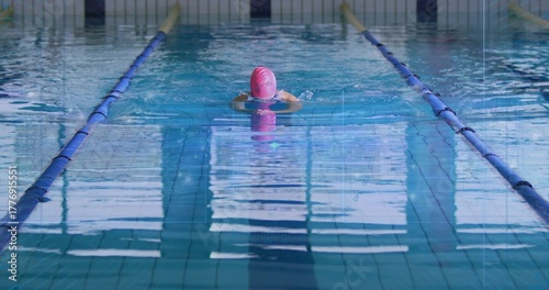 Swimming woman performing breaststroke in pool lane, with pink swim cap and blue lane dividers