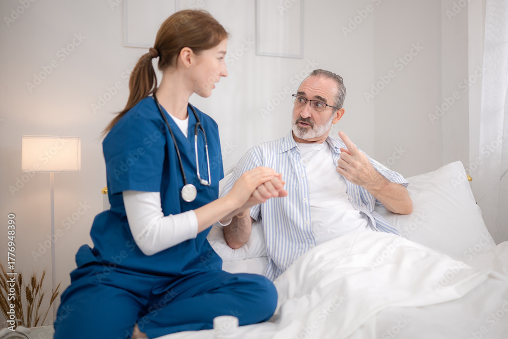 Fototapeta premium Female nurse assisting an elderly patient in bed while reviewing medical information