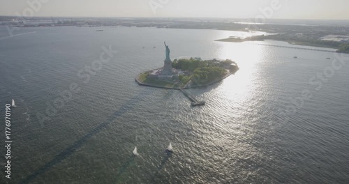 Cinematic silhouetted shot of beautiful statue of liberty on island with surrounding boats, helicopter shot