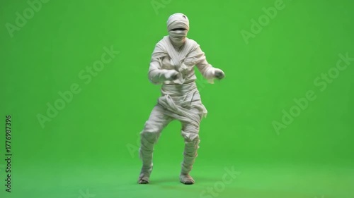 A person in a mummy costume dances against a solid green background