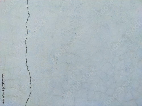 Texture of a painted wall in pale blue-gray, characterized by a long, pronounced vertical crack running down the left side and subtle hairline cracks across the surface, creating an abstract and aged.