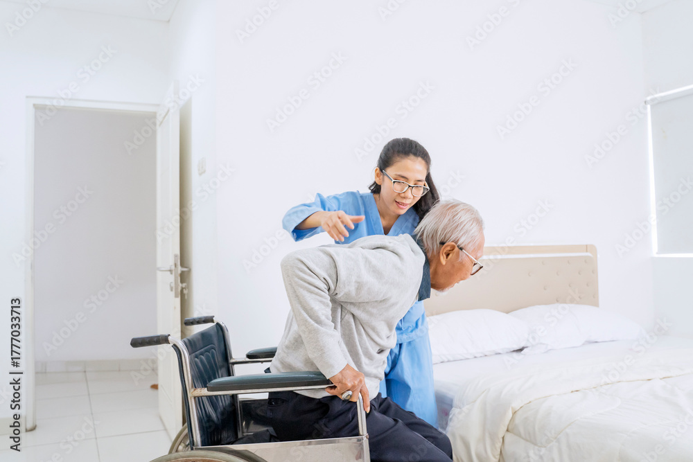 Obraz premium Professional Nurse Helping Elderly Man Transfer from Wheelchair to Bed