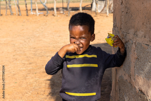 hungry african child in the village, eating biscuits next to the house in the yard
