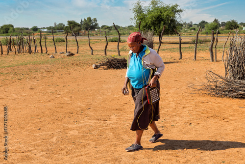 village old african woman using a solar panel with radio, to recharge phones and light, donated by a charity NGO, to improve life in rural areas