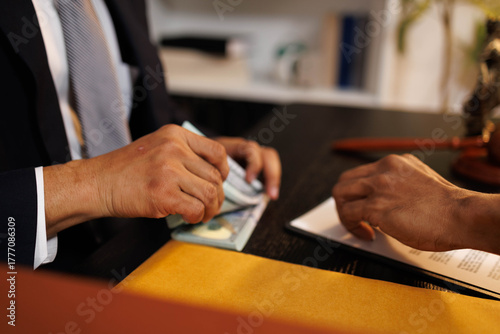 A man is handing a stack of money to another man. The man receiving the money is wearing a suit and tie. The scene appears to be a business transaction or negotiation

