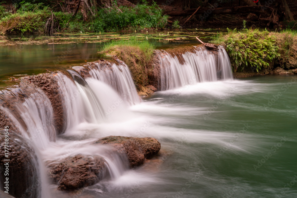 Obraz premium Cascading Beauty: A serene view of a small waterfall gracefully cascading over rocky formations, creating a tranquil atmosphere, emphasizing the beauty of water and nature's artistry.