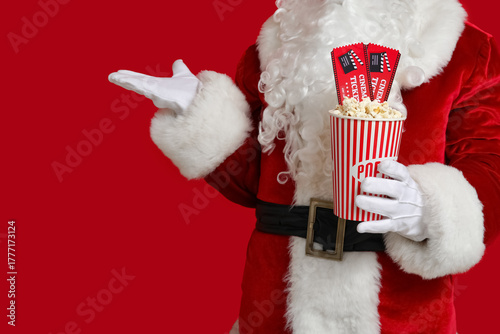 Santa Claus with bucket of popcorn and cinema tickets on red background. Closeup