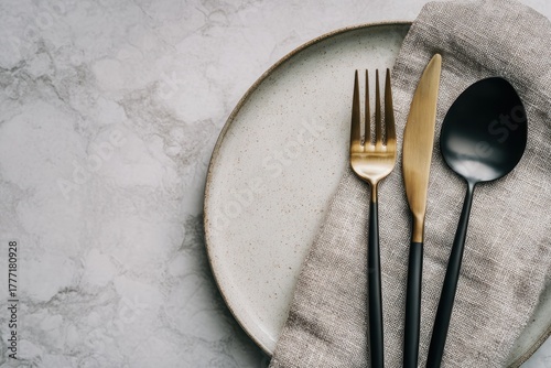 Elegant Dining Setup: A Stylish Plate with Golden Cutlery and a Textured Napkin for Modern Table Settings