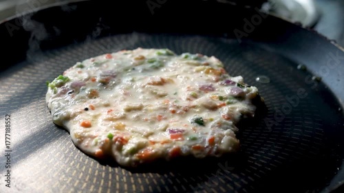 Indian chilla or uttapam prepared on black pan in kitchen with sunlight