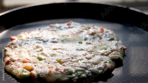 Indian chilla or uttapam prepared on black pan in kitchen with sunlight