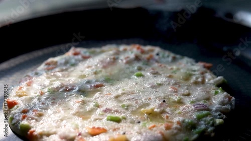 Indian chilla or uttapam prepared on black pan in kitchen with sunlight