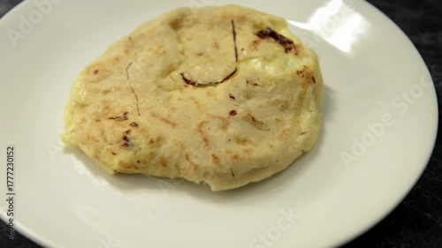 A close-up parallax pan video of a cheese pupusa on a white plate against a black-grey marble background.
