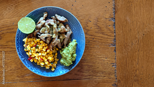 pork fajitas, corn and guacamole on a blue plate with a rustic oak wood background  
