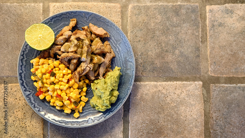 pork fajitas, corn and guacamole on a blue plate with a rustic tiled background  