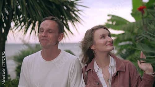 Romantic young couple in 30s talking and walking along a tropical seaside at sunset. Palm trees, golden light, and calm blue ocean 