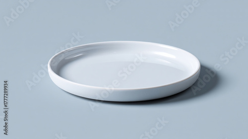 A minimalist white ceramic plate on a light gray surface casting a soft shadow to the right side