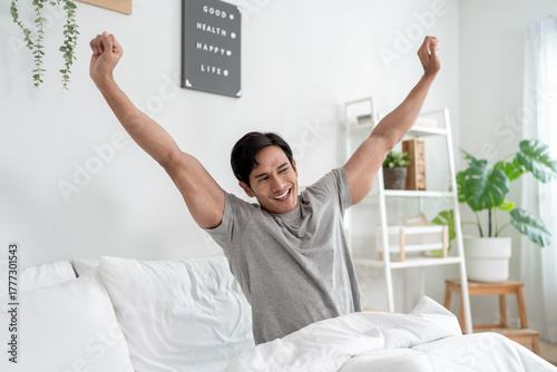 Asian handsome young man getting up from sleep on bed in the morning.