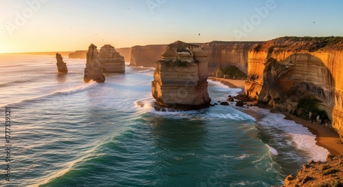Coastal view featuring rock formations in the ocean at sunset with waves, sand, & distant horizon