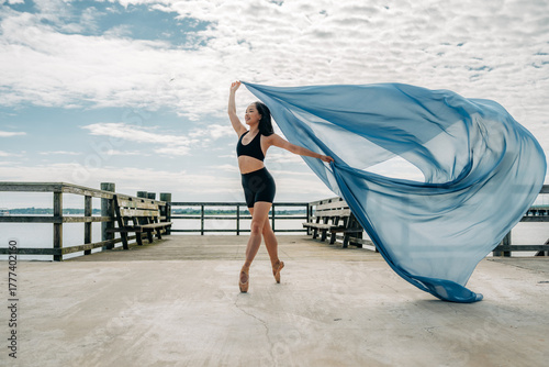 Ballet dancer twirls on pier with large flowing blue fabric