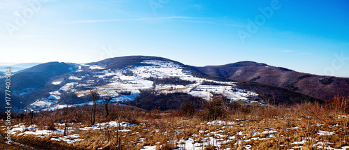 A wide panoramic view of rolling hills partially covered in late winter snow and patchy brown grass.