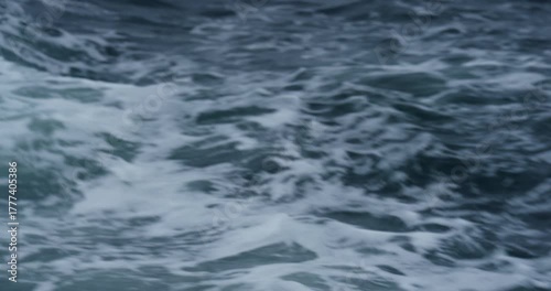 Foamy azure water trail rolls behind sailing fast motorboat at seaside. Ocean waves and splashes creates abstract pattern on rough surface