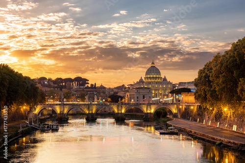 View of the Tiber River reflecting the golden sunset light illuminating the iconic St. Peter's Basilica and Ponte Sant'Angelo, Rome, Lazio, Italy.