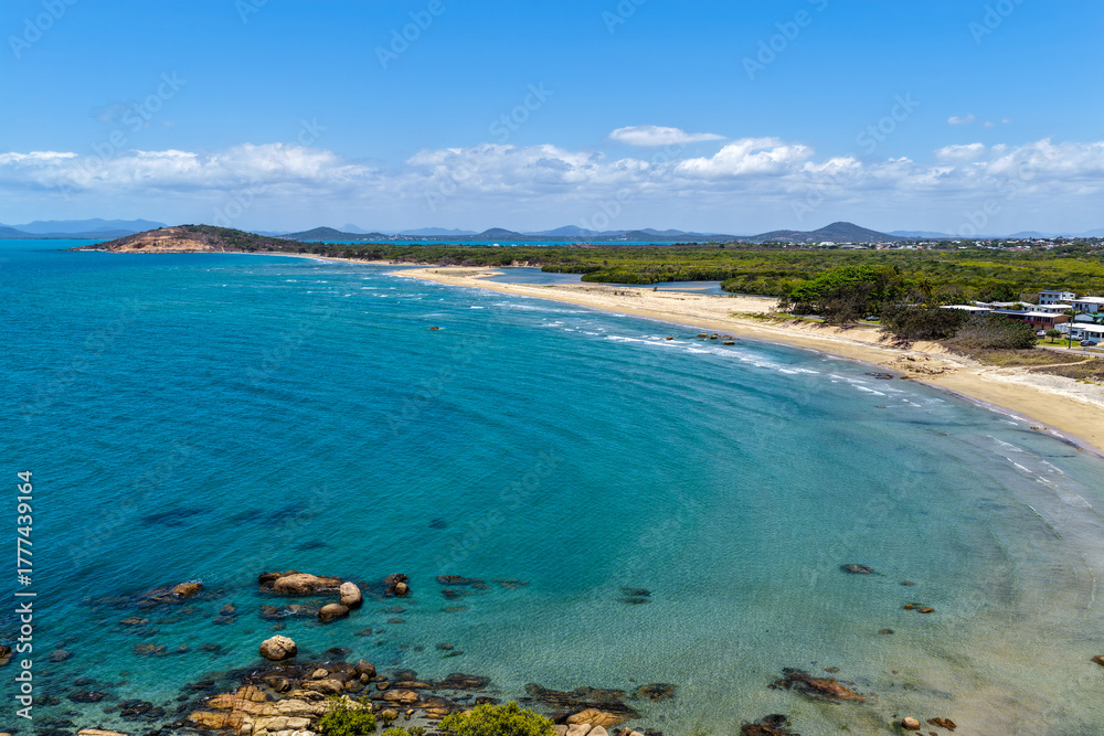 Obraz premium An aerial view of Rose Bay in Bowen, Queensland, reveals a stunning tropical coastline with turquoise waters, golden sand, and rocky headlands. The scene highlights coastal beauty and vibrant color.