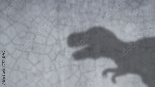 Blurred shadow of dinosaur shown on empty flat polished cement wall background.