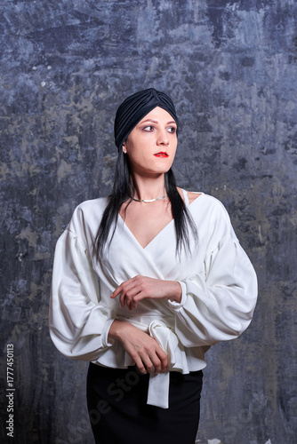 In a dark room stands a beautiful girl with long hair, dressed in a black leather skirt and a white blouse. Her outfit is designed in a business style. This is the image of a business woman.