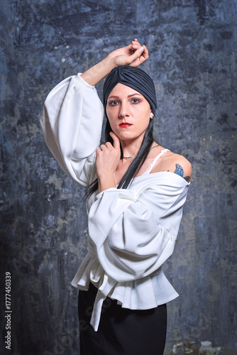 In a dark room stands a beautiful girl with long hair, dressed in a black leather skirt and a white blouse. Her outfit is designed in a business style. This is the image of a business woman.