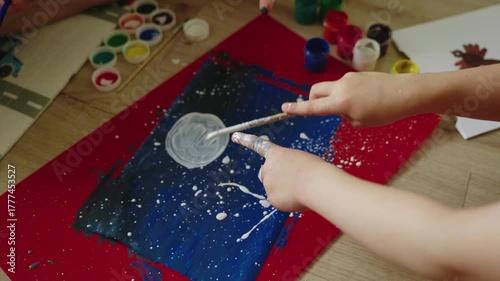 Young artist applies paint splatter technique on canvas, showcasing creativity and motion