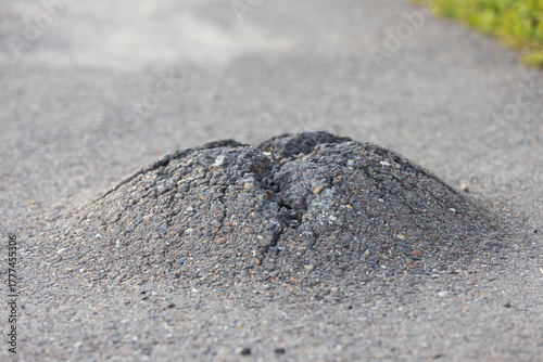 Close-up of frost heave on asphalt surface. Damage in the asphalt surface of sidewalk is like a volcano crater or anthill