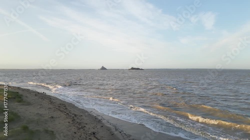 Drone flying over sandy beach and sea water to tidal island Mont-Saint-Michel in Normandy France in morning sunrise. Aerial footage of medieval abbey on skyline during high tide