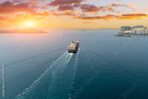Large container ship sails out of the bay and strait into the sunrise far away with a beautiful sunlit landscape on the horizon