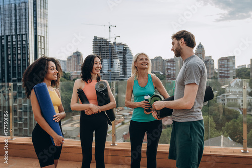 Happy multiracial group of bearded man and women discusses yoga lesson at hotel terrace