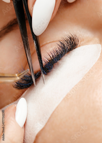 Close-up of a beauty professional applying eyelash extensions with precision tweezers, showcasing the intricate process of lash enhancement and beauty care techniques