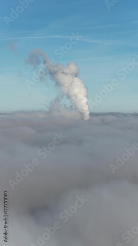 Aerial drone view of industrial chimneys emitting steam above thick fog and clouds on a sunny day, power plant and factory landscape. Panorama above clouds in fog in sunny day. Clouds factory