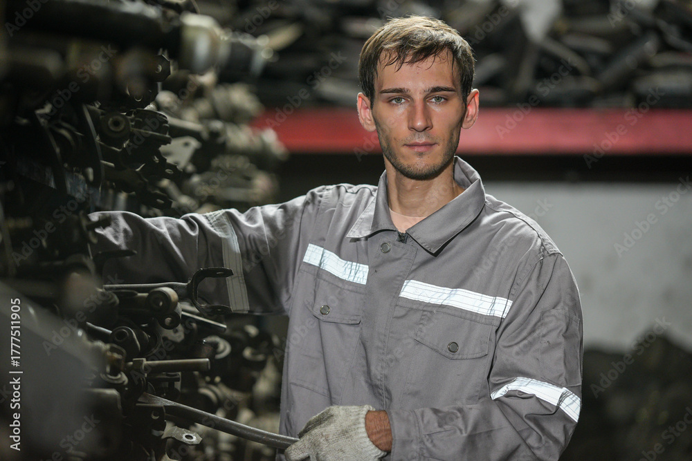 Fototapeta premium White man technician checking used car damaged engine block at scrap yard warehouse recycle area part. Maintenance engineer inspecting rust oily auto motor old spare part in junkyard for reuse service
