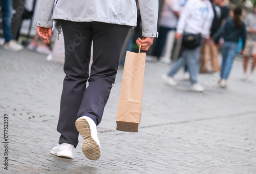 Menschen unterschiedlichen Alters beim Einkaufen mit in der Stadt – selektiver Fokus auf eine Frau im Vordergrund mit einer Einkaufstüte in der Hand, viel Copyspace