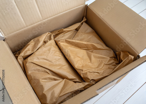 Cardboard container with wrinkled brown packing paper for protection, flaps open to reveal cushioning material inside, perfect for shipping and packing. 