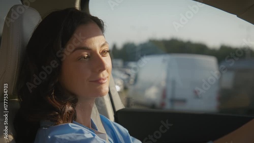 Charming Caucasian woman with wavy dark hair driving car during sunset time. Female focused on road while sunlight gently illuminates face. Peaceful evening ride back home in countryside.