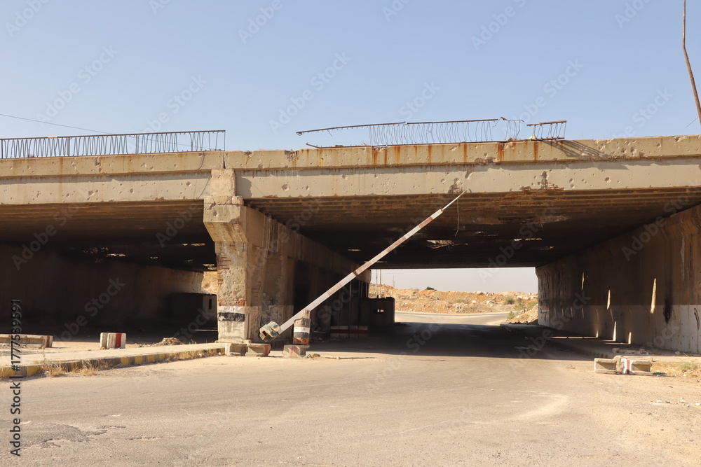 Obraz premium Abandoned former Syrian army checkpoint under a damaged bridge near Aleppo, Syria. symbolizing war’s end and the rise of freedom. Ideal for documentaries, news and archives on Middle Eastern conflicts