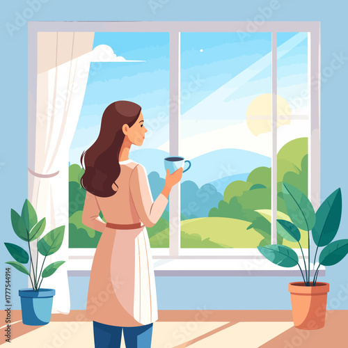 Young woman with long brown hair, wearing a casual robe and jeans, holding a blue coffee cup while standing in a relaxed, contemplative pose.